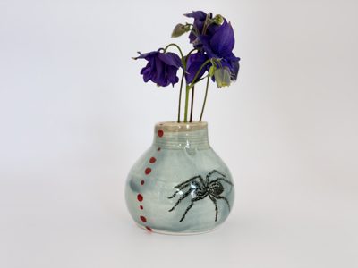 Bud vase with a spider illustration, holding purple flowers